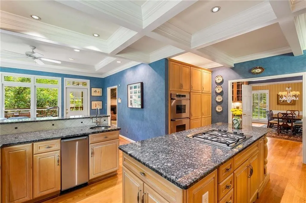 Kitchen with coffered ceiling, beamed ceiling, light wood-style flooring, crown molding, and appliances with stainless steel finishes - view towards formal dining room.