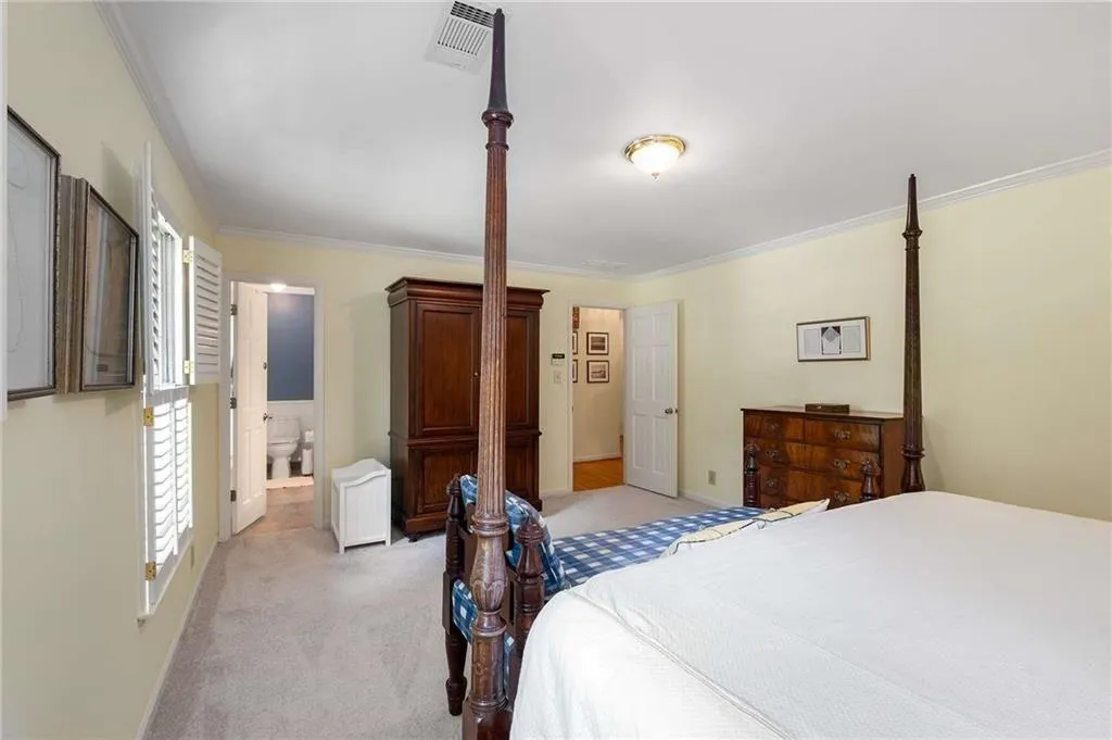 Bedroom with light colored carpet, ornamental molding, and ensuite bath