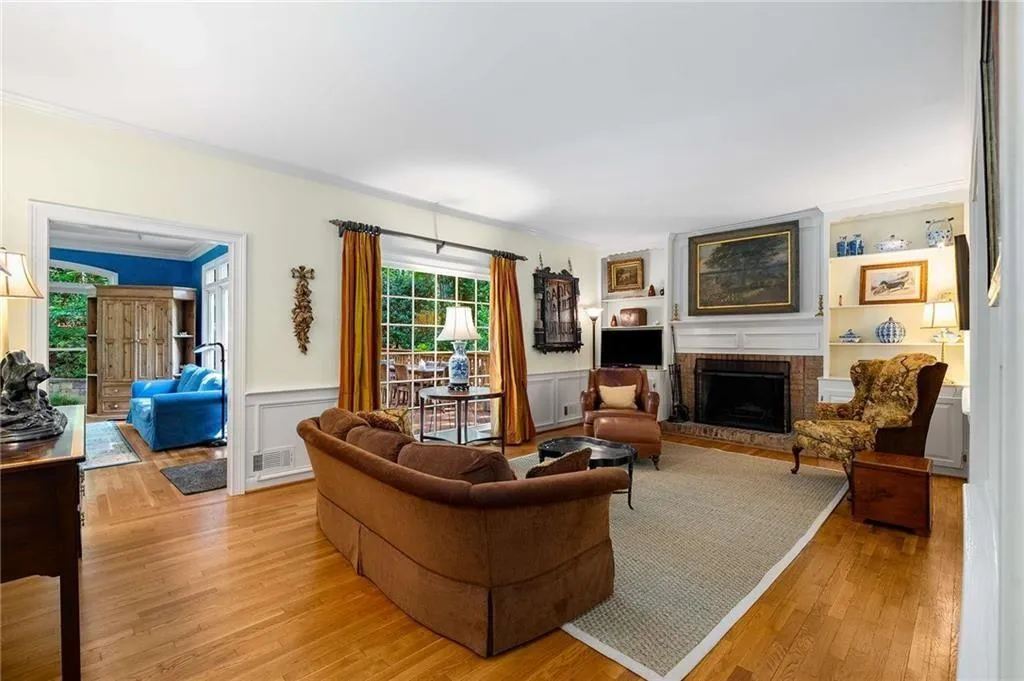 Family room with high ceilings, lots of light, a masonry brick fireplace, hardwood flooring, crown molding, a wainscoted wall, and view towards den and deck.