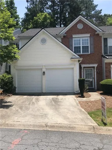 Two-car attached garage, brick facade with white siding, arched window in gable, front door with decorative glass, and concrete driveway