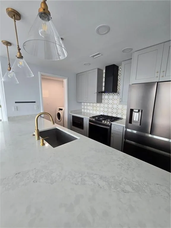 Kitchen with stove, refrigerator, washer / clothes dryer, ventilation hood, and backsplash