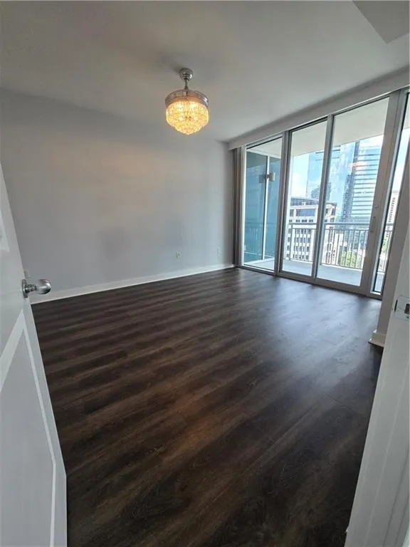 Unfurnished room with dark wood finished floors, a chandelier, and floor to ceiling windows