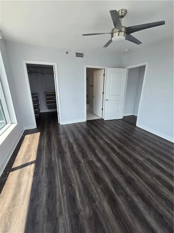 Unfurnished bedroom featuring dark wood-type flooring, a spacious closet, and a ceiling fan