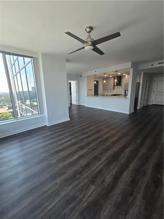 Unfurnished living room featuring a ceiling fan and dark wood-style floors