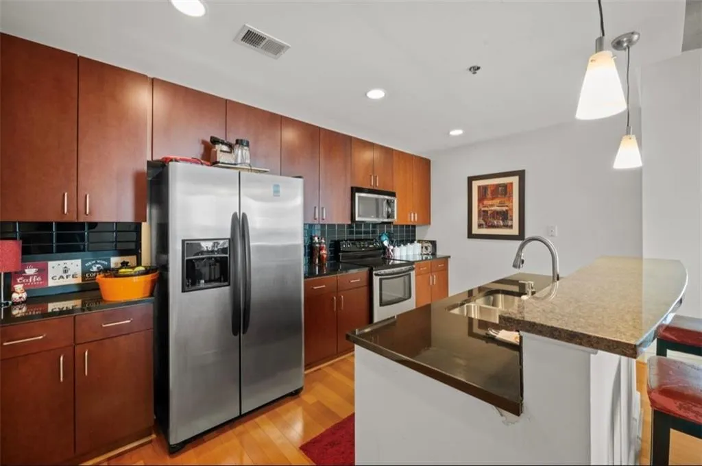 Kitchen with appliances with stainless steel finishes, hanging light fixtures, dark stone counters, recessed lighting, and a peninsula