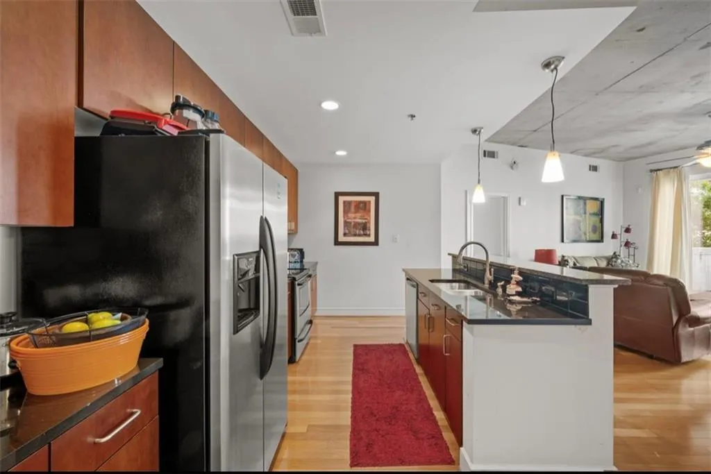 Kitchen with stainless steel appliances, open floor plan, brown cabinetry, dark stone countertops, and recessed lighting