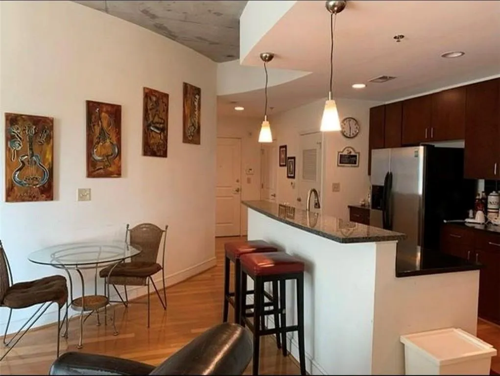 Kitchen with dark brown cabinetry, an island with sink, stainless steel refrigerator with ice dispenser, a kitchen breakfast bar, and light wood-type flooring