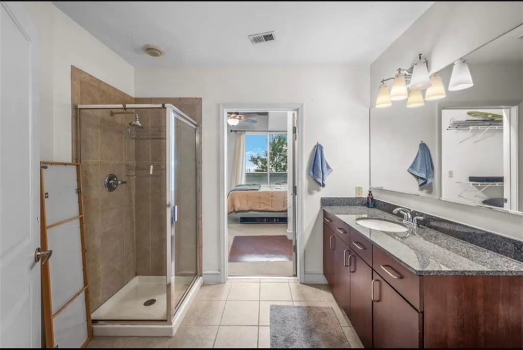 Ensuite bathroom featuring vanity, a shower stall, light tile patterned floors, ceiling fan, and a closet