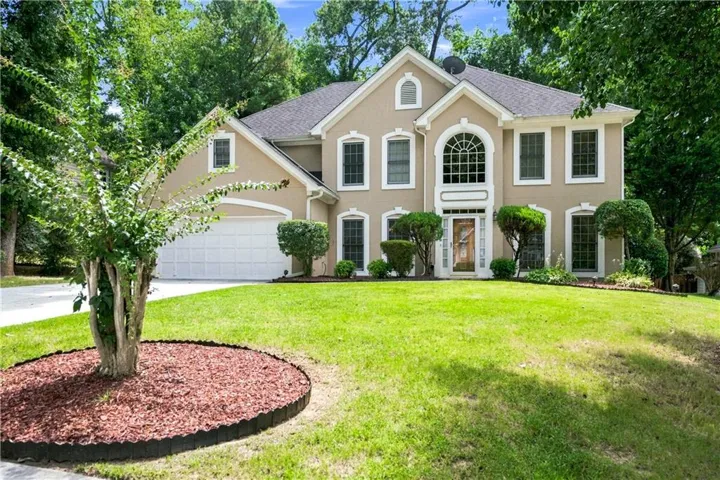 Stucco exterior with arched entry window, double garage, and a manicured lawn