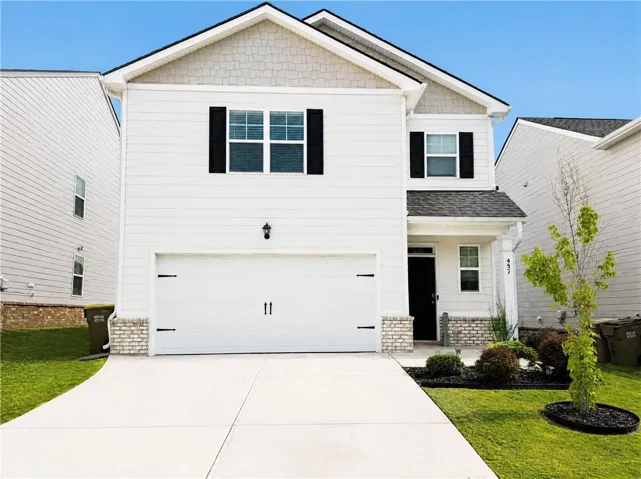 Two-story home with white siding, dark shutters, an attached garage, a concrete driveway, and landscaped front yard