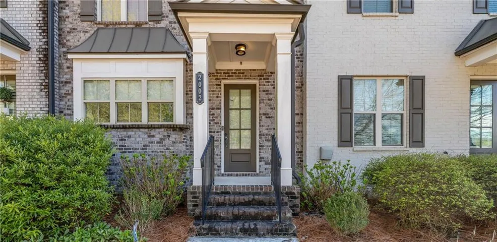Brick facade with white painted brick accents, covered entry with substantial columns, dark-framed multi-pane windows, and decorative dark shutters
