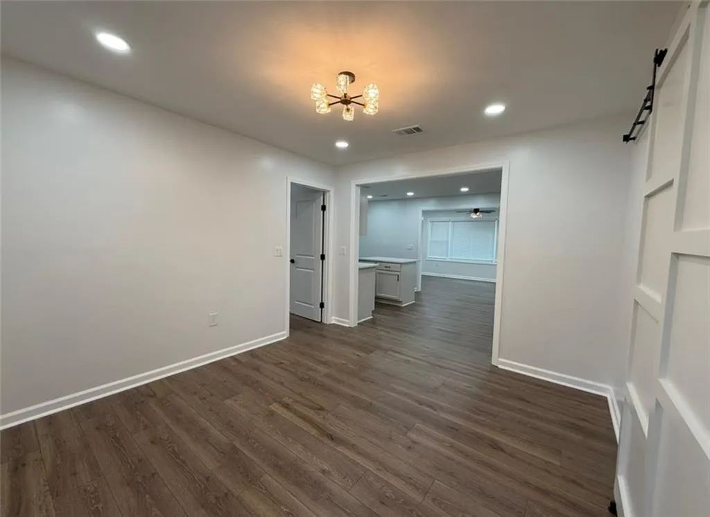 Unfurnished dining area with dark wood-type flooring, recessed lighting, a barn door, and a chandelier