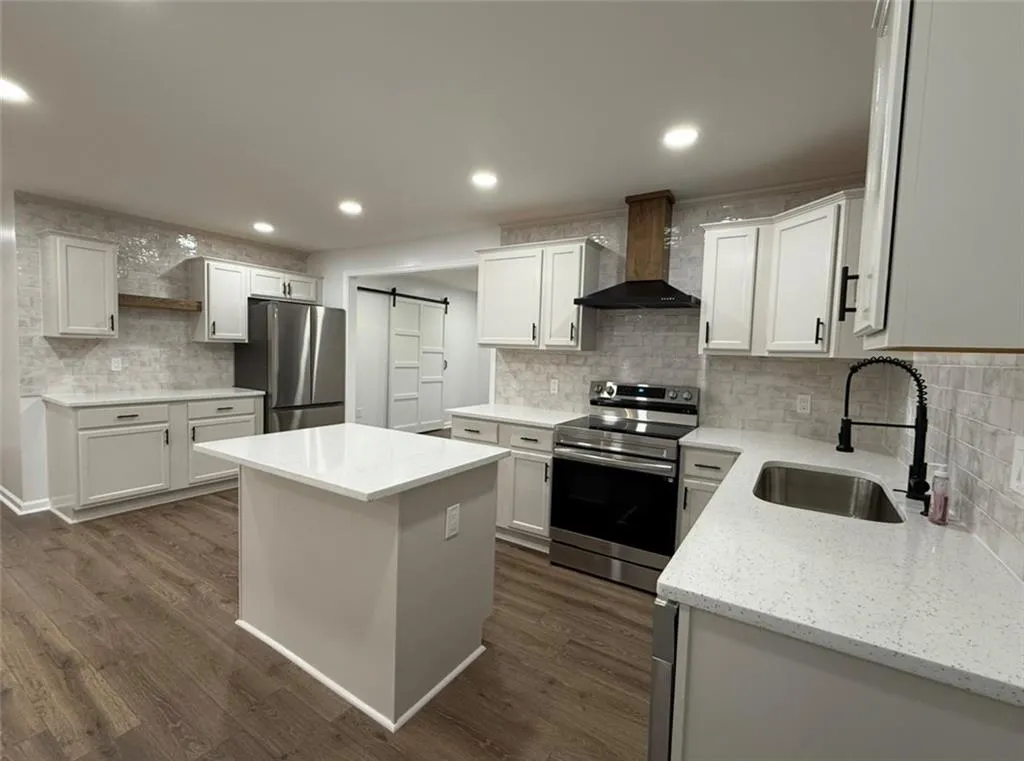 Kitchen featuring a barn door, stainless steel appliances, wall chimney range hood, recessed lighting, and white cabinets