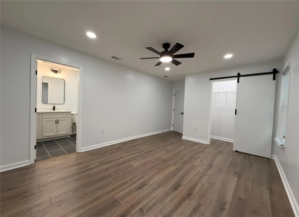 Unfurnished bedroom featuring a barn door, dark wood finished floors, a spacious closet, recessed lighting, and a ceiling fan