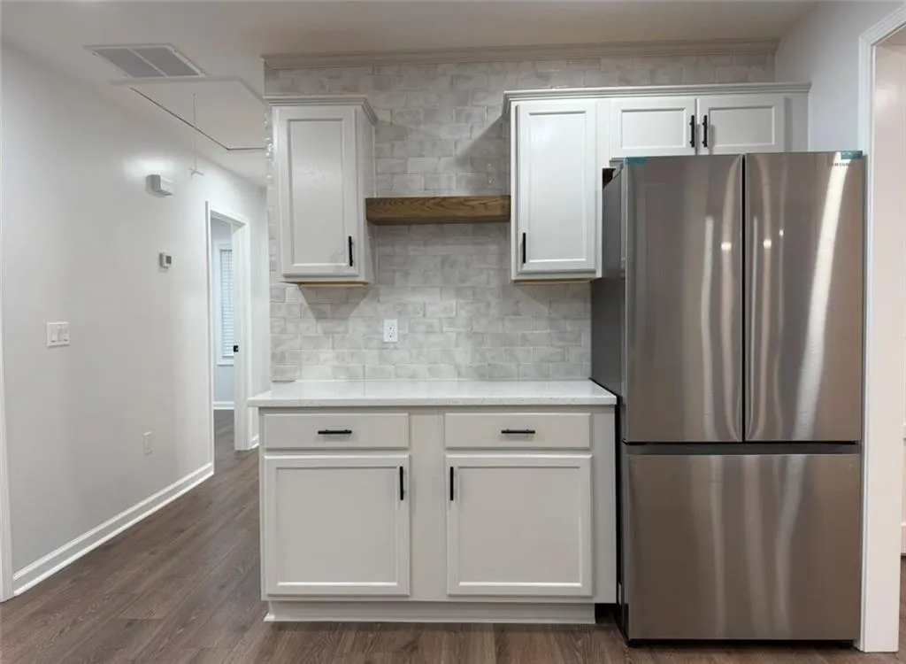 Kitchen with freestanding refrigerator, dark wood-style flooring, white cabinets, light stone countertops, and backsplash