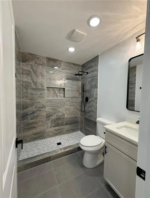 Bathroom with vanity, a walk in shower, dark tile patterned floors, and recessed lighting