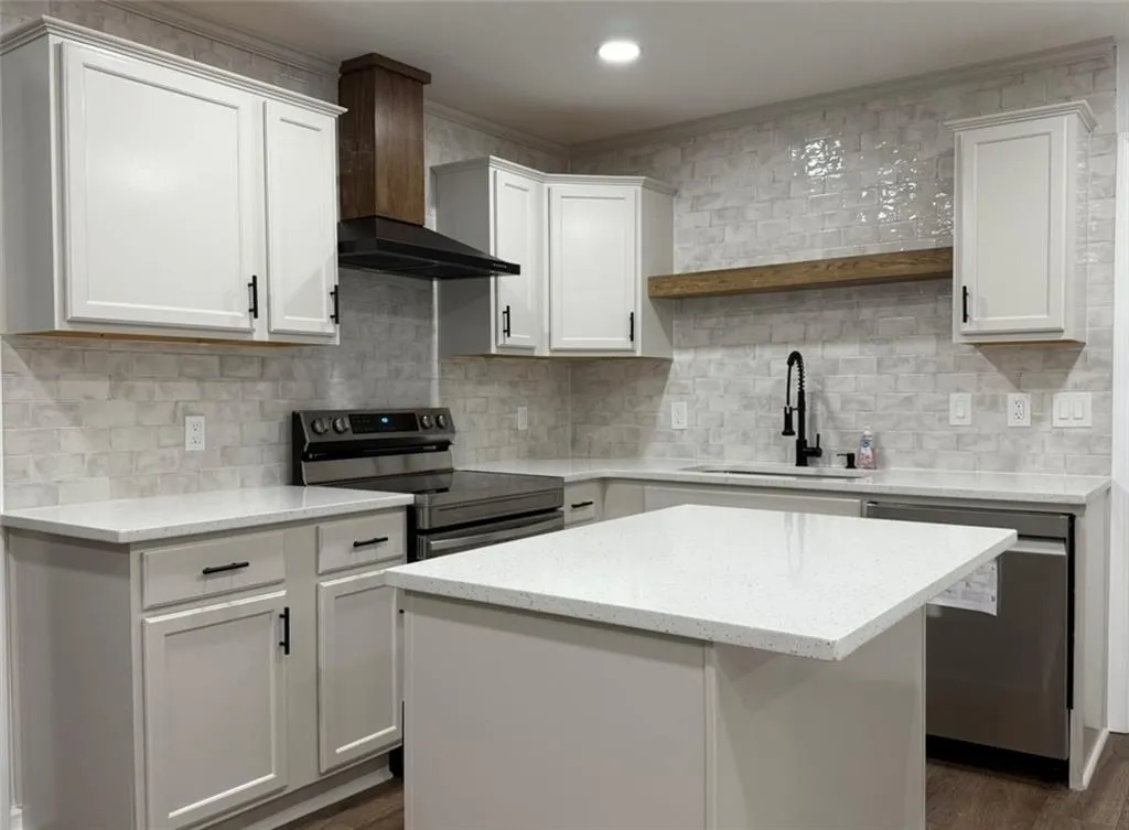 Kitchen with appliances with stainless steel finishes, wall chimney range hood, white cabinets, light stone counters, and decorative backsplash