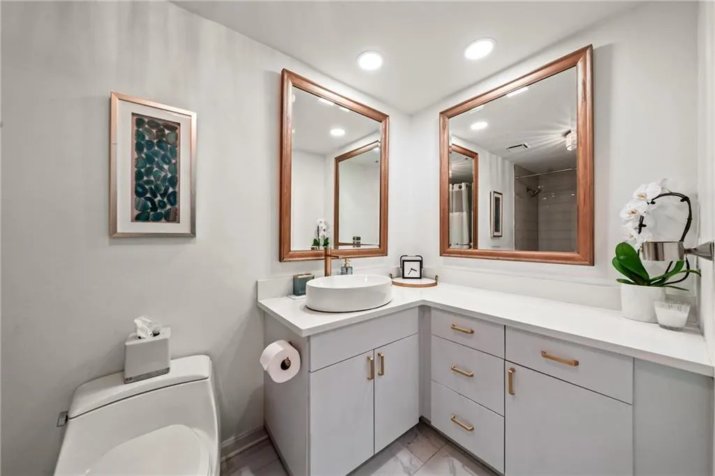 Spa-inspired dual-sink vanity featuring white vessel sinks, soft-close cabinetry with warm wood-tone hardware, quartz countertops, and framed mirrors with wood accents