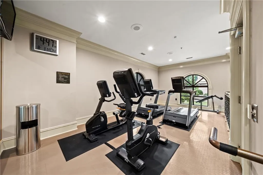 Dedicated fitness room featuring multiple stationary bikes with individual digital displays, premium rubber flooring, recessed lighting throughout, and abundant natural light from arched transom windows