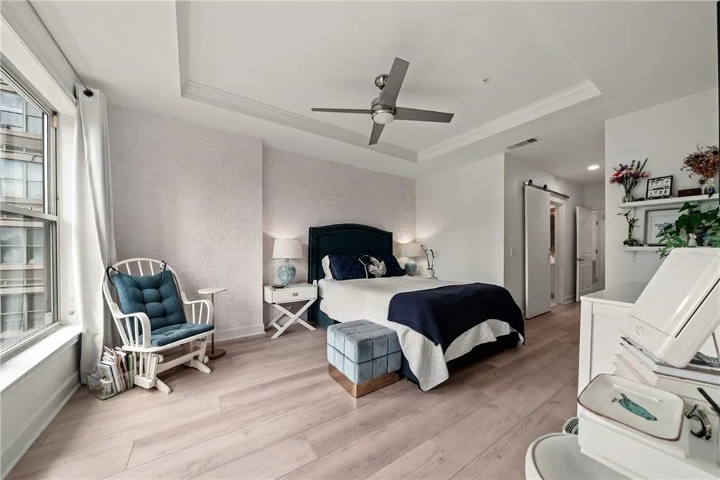 Spacious primary bedroom featuring a coffered ceiling with integrated ceiling fan, wood-finish flooring throughout, and abundant natural light from large windows