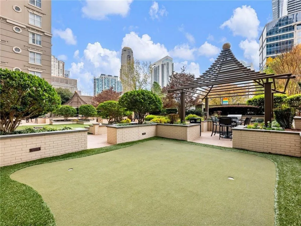 Expansive putting green with meticulously manicured synthetic turf, bordered by raised planter beds with mature landscaping