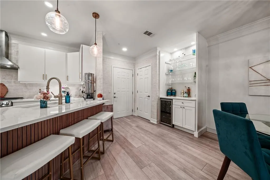 Sophisticated kitchen and dining area featuring a custom wood-finish island with seating for three, white cabinetry with integrated appliances, quartz countertops, pendant lighting, and wood-finish flooring throughout