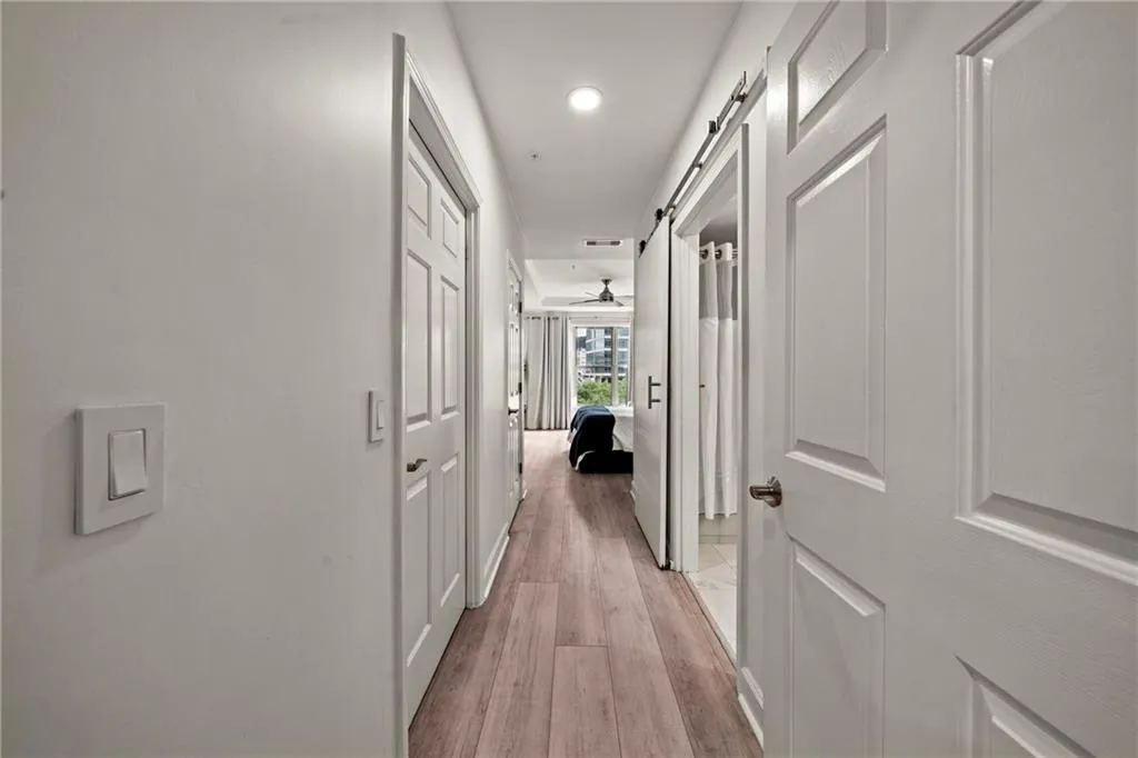 Elegant hallway featuring pristine white six-panel doors, recessed ceiling lighting, polished wood-finish flooring, and clean white walls with modern light switch plates throughout