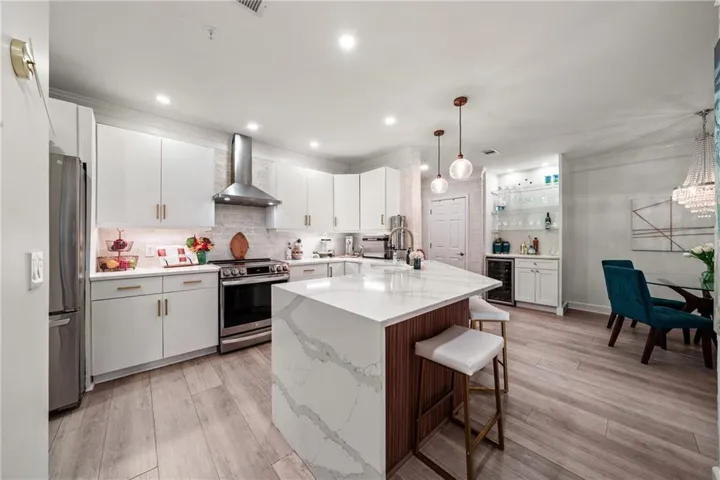 Kitchen featuring a quartz-top island with wood-finish paneling, white cabinetry with gold-tone hardware, stainless steel range with a ventilation hood, and wood-finish flooring