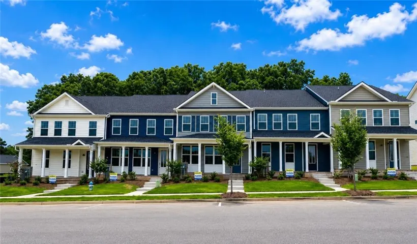 Row of townhomes featuring varied exterior siding colors, covered porches with white columns, gabled rooflines, and front lawns with mature trees