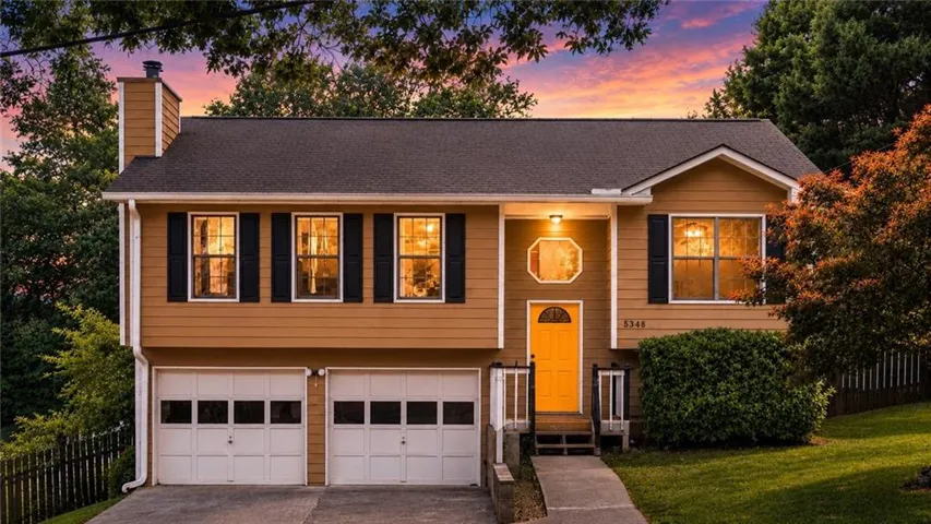 Split-level home featuring a two-car garage with panel doors, a vibrant yellow front door, and a shingled roof
