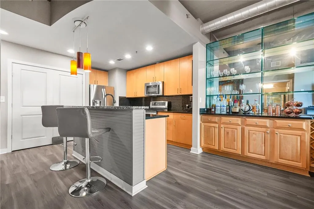 Kitchen featuring tasteful backsplash, hanging light fixtures, an island with sink, a breakfast bar, and dark wood-type flooring Kitchen featuring tasteful backsplash, hanging light fixtures, an island with sink, a breakfast bar, and dark wood-type flooring