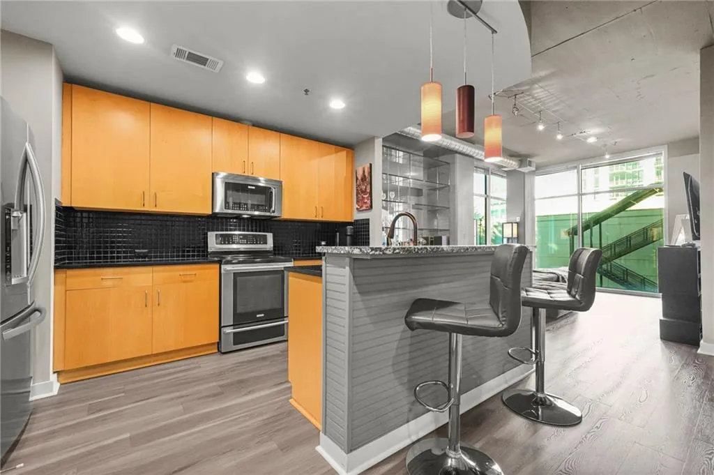 Kitchen featuring a kitchen breakfast bar, stainless steel appliances, pendant lighting, light wood-type flooring, and decorative backsplash Kitchen featuring a kitchen breakfast bar, stainless steel appliances, pendant lighting, light wood-type flooring, and decorative backsplash