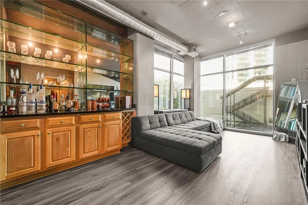 Indoor bar featuring brown cabinets, open shelves, dark wood-style flooring, expansive windows, and dark stone countertops Indoor bar featuring brown cabinets, open shelves, dark wood-style flooring, expansive windows, and dark stone countertops