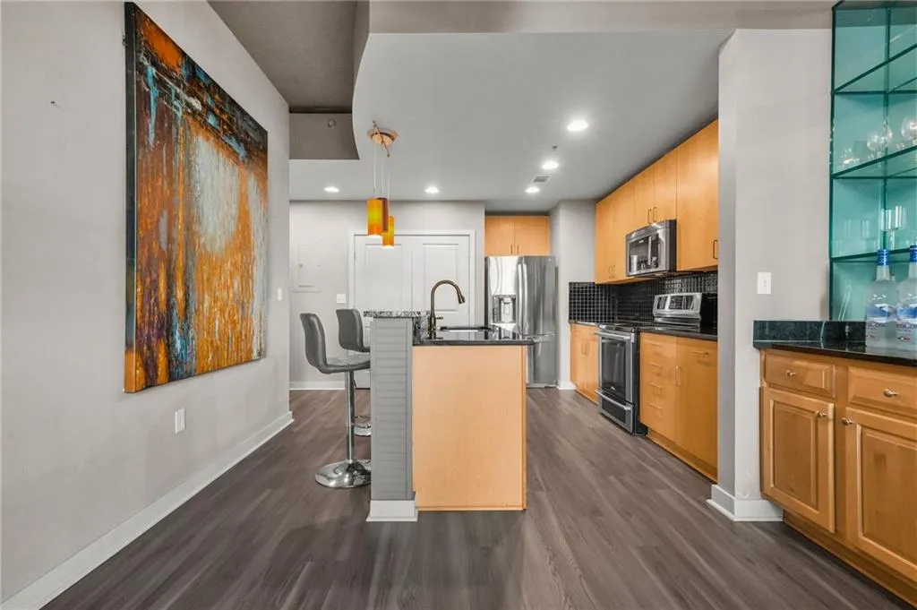 Kitchen with appliances with stainless steel finishes, decorative light fixtures, dark wood-type flooring, a kitchen breakfast bar, and recessed lighting Kitchen with appliances with stainless steel finishes, decorative light fixtures, dark wood-type flooring, a kitchen breakfast bar, and recessed lighting