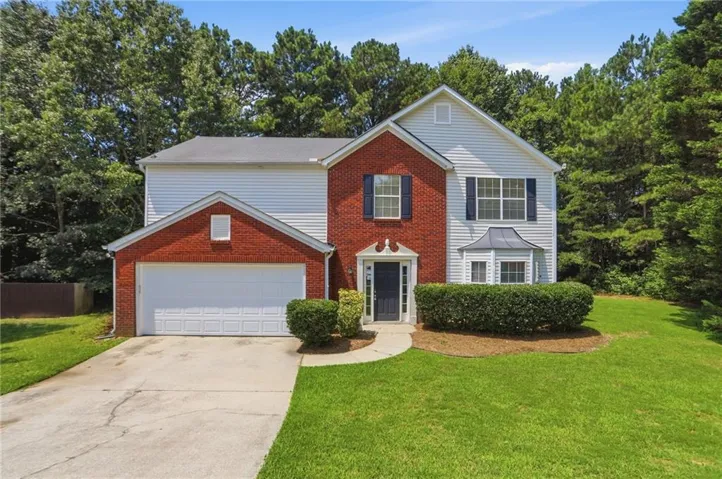Two-story residence featuring a brick and siding exterior, a two-car garage, and a bay window with a metal canopy