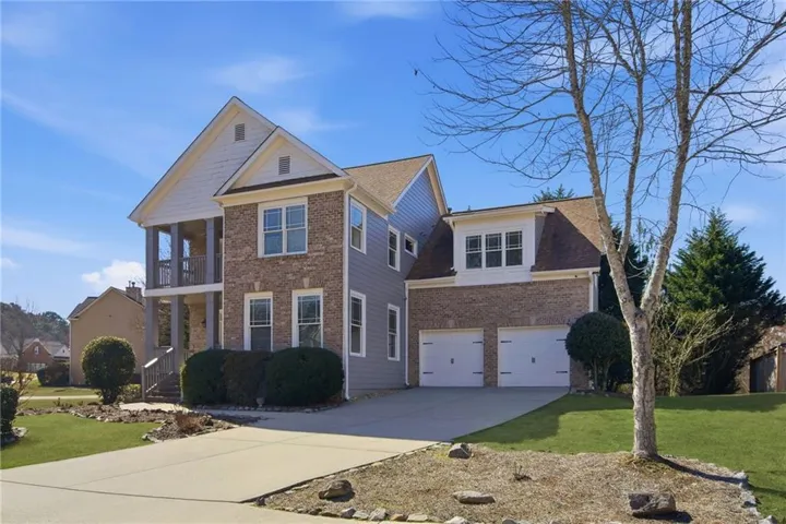 Two-story residence featuring a brick and siding exterior, a two-car garage, and a covered balcony