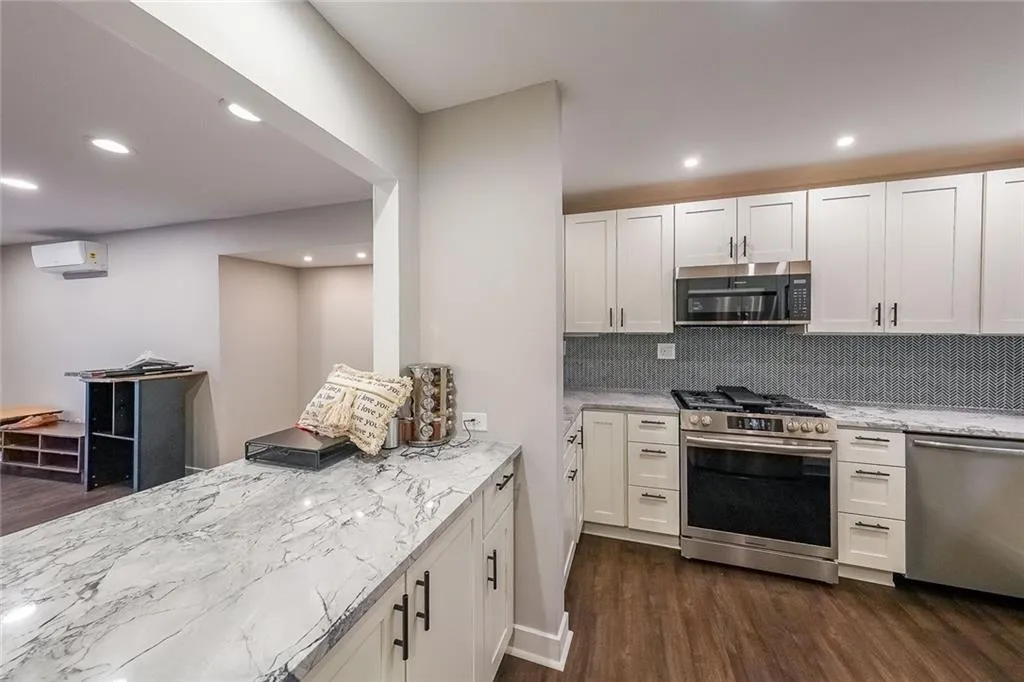 Kitchen with dark wood finished floors, an AC wall unit, light stone counters, and stainless steel appliances