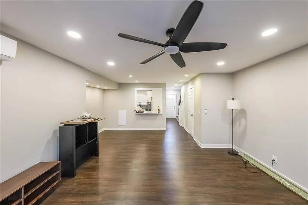 Living room with a wall unit AC, a ceiling fan, dark wood-style floors, baseboards, and recessed lighting