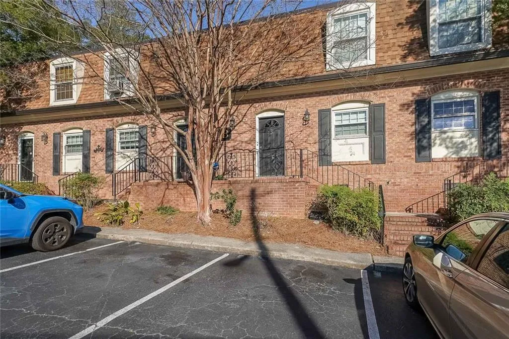 View of property with brick siding, mansard roof, and uncovered parking