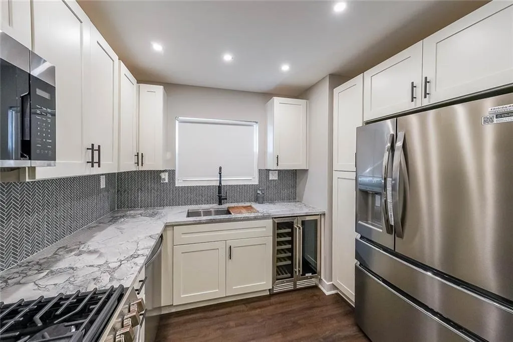 Kitchen with dark wood-type flooring, light stone counters, white cabinets, stainless steel appliances, and a sink