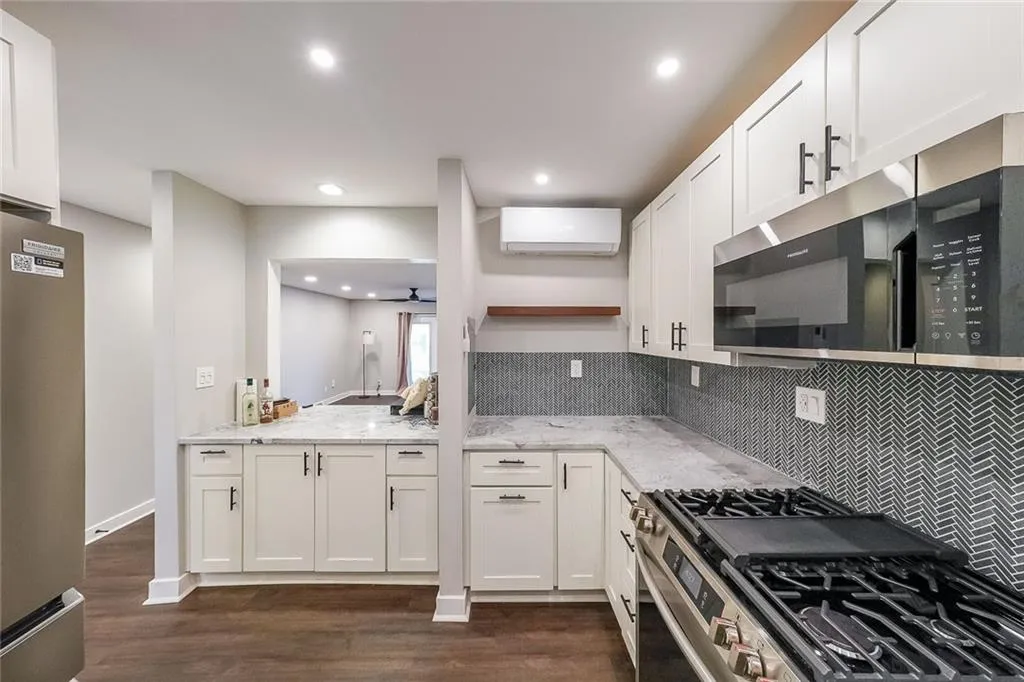 Kitchen featuring light stone counters, a wall mounted AC, open shelves, appliances with stainless steel finishes, and white cabinetry