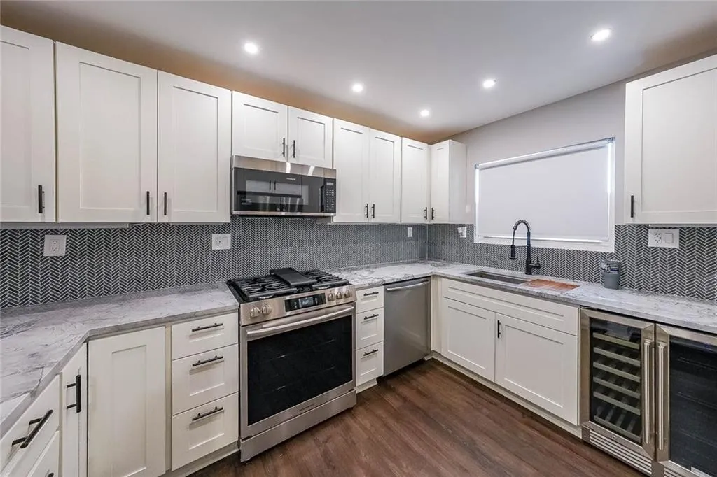 Kitchen featuring dark wood-type flooring, a sink, white cabinetry, stainless steel appliances, and wine cooler