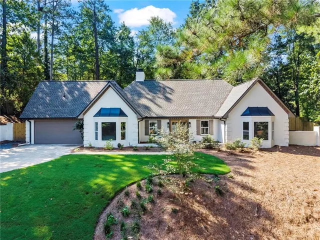 White stucco exterior with a gray shingle roof, attached garage, and a manicured front lawn
