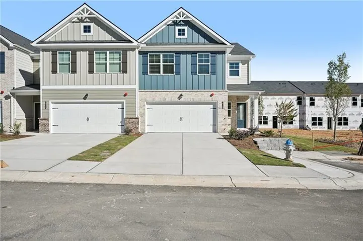 Contemporary townhome facade featuring board and batten siding, brick accents, dual single-car garages, a covered entry, and a gabled roofline