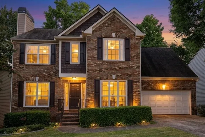 Brick exterior with shuttered windows, a paneled garage door, and a covered entry