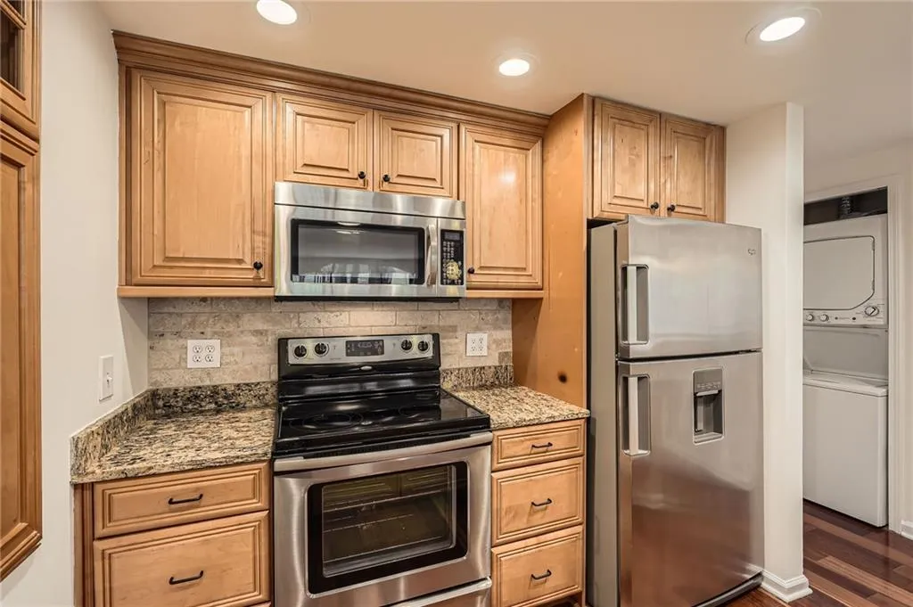 Kitchen featuring stacked washer and clothes dryer, backsplash, dark wood-style floors, and stainless steel appliances