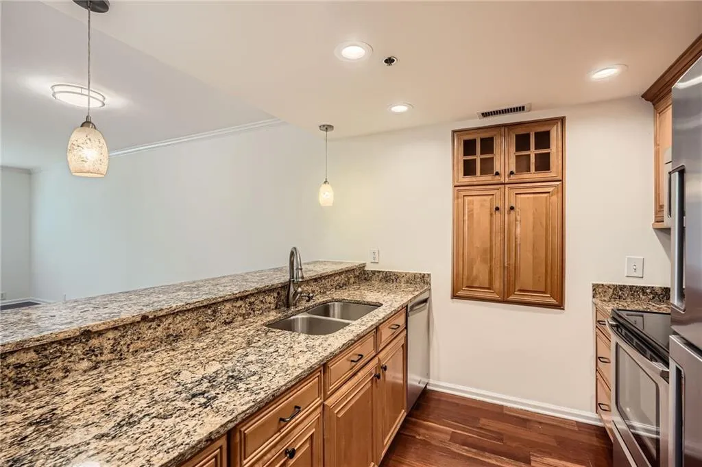 Kitchen with a sink, brown cabinetry, appliances with stainless steel finishes, light stone countertops, and dark wood-style floors