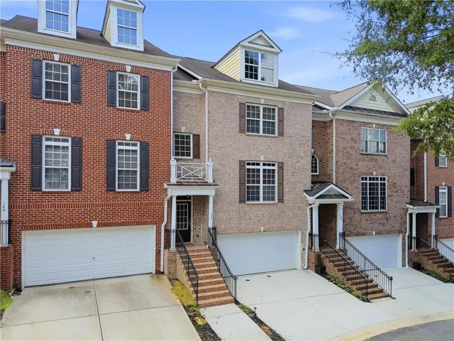 Brick exterior with dormer windows, individual garage, and a covered entry with railings