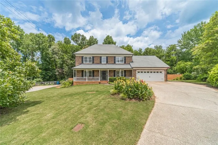 Traditional brick home featuring a covered front porch with white railings, a front-facing attached garage, and a long paved driveway