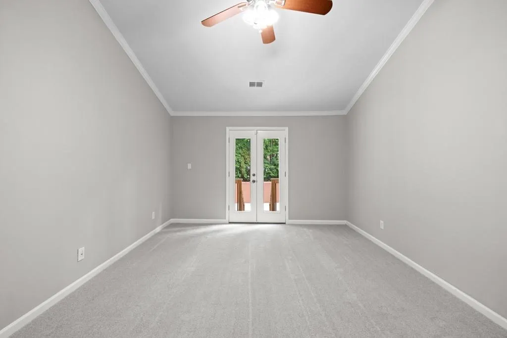 Carpeted empty room featuring crown molding, ceiling fan, and french doors